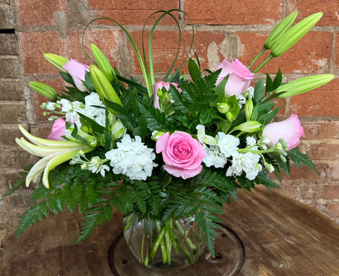 Luxurious fresh pink roses and white lilies bouquet in clear glass vase on wooden table, premium online flower delivery arrangement by Floward showcasing vibrant blooms for special occasions in the Middle East and UK 2026.